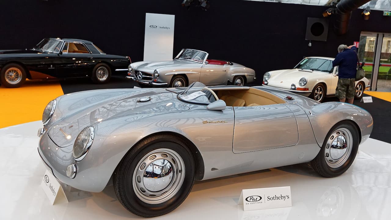 Silver 1955 Porsche 550 Spyder roadster with open cockpit and chrome wheels displayed at Sotheby's auction showroom