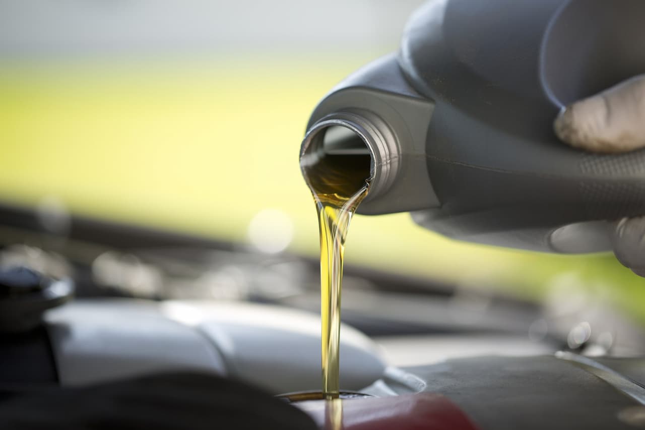 Hand pouring golden motor oil from black bottle into car engine during automotive maintenance in service garage