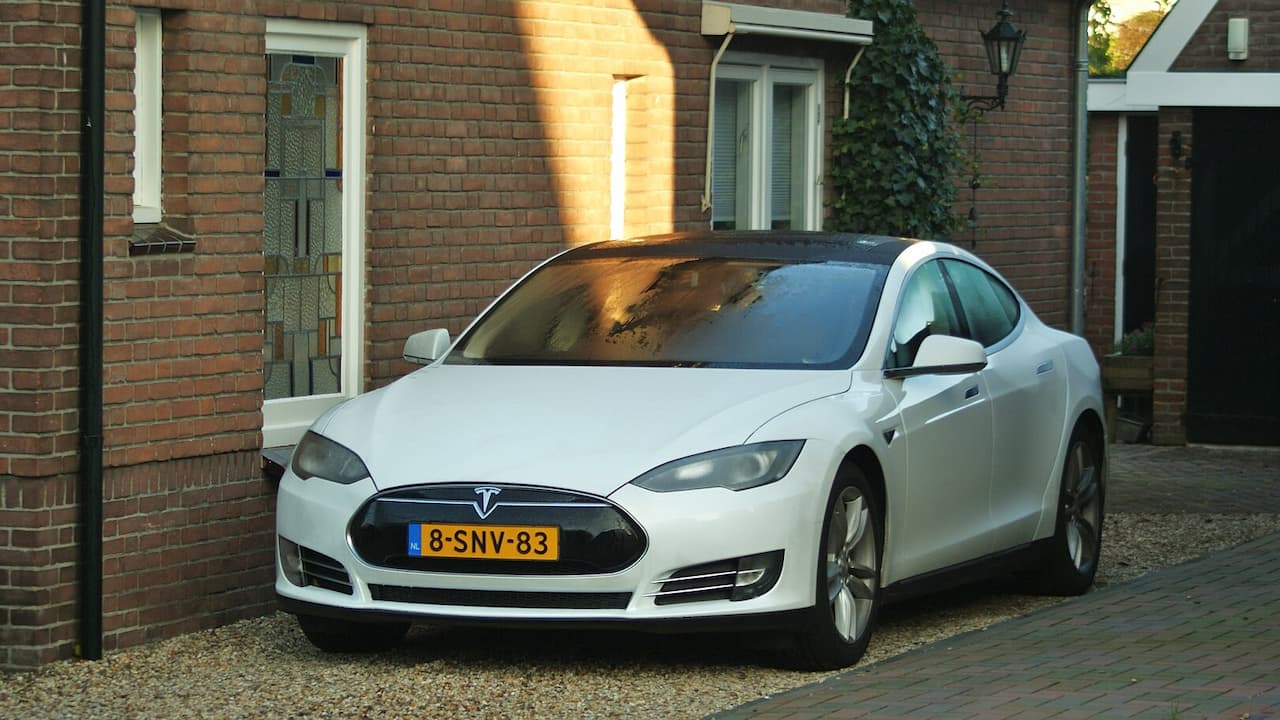 White 2012 Tesla Model S with Dutch license plate parked in residential driveway beside brick house
