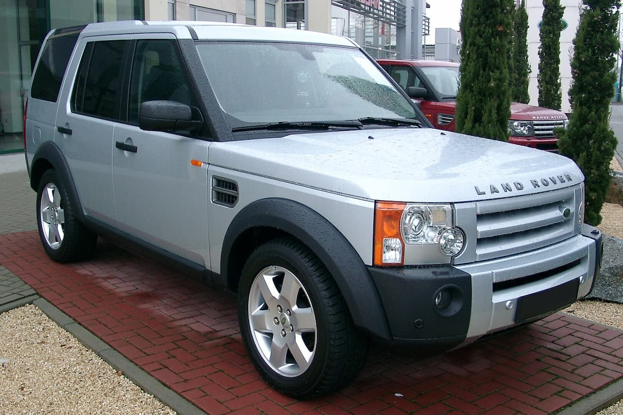 Silver Land Rover Discovery with black plastic cladding parked on brick pavement outside modern building
