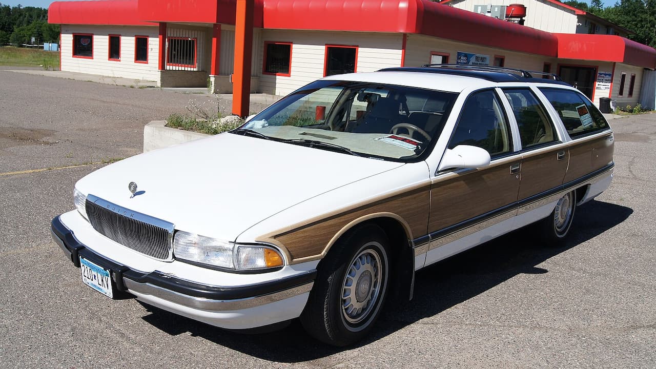 White Buick Roadmaster Estate station wagon with wood paneling parked outside red and white commercial building