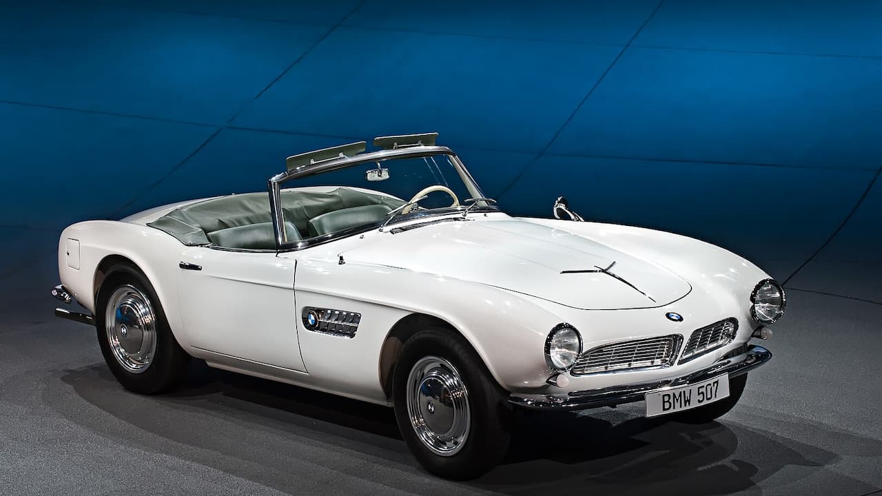 White 1956 BMW 507 Roadster with chrome details, wire wheels, and green leather interior on display