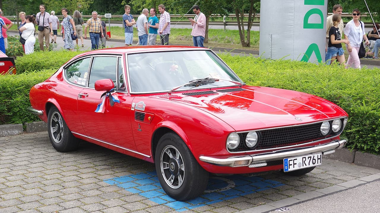 Red Fiat Dino with quad headlights and German license plate displayed at outdoor car show