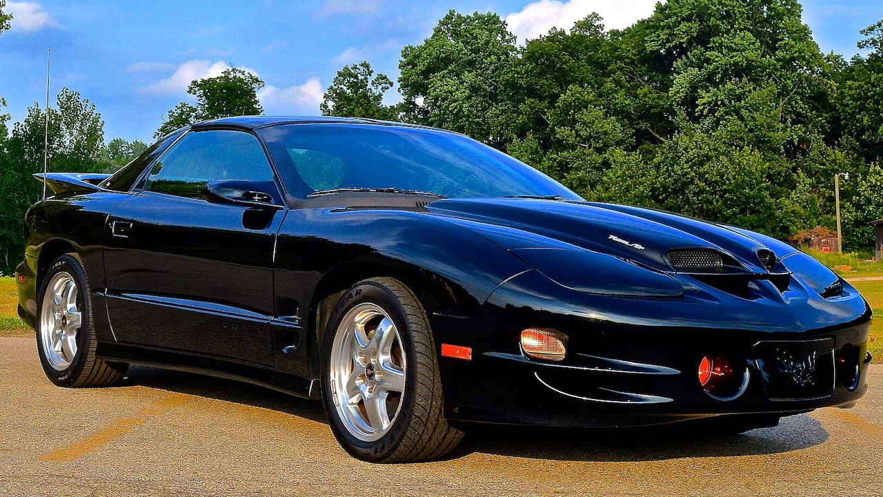 Black 2002 Pontiac Firebird Trans Am WS6 with hood scoops and chrome wheels parked on asphalt road
