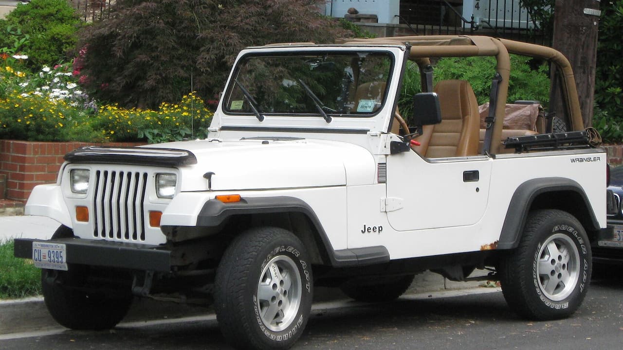 White Jeep Wrangler with tan soft top and roll bars parked on residential street with flowers nearby