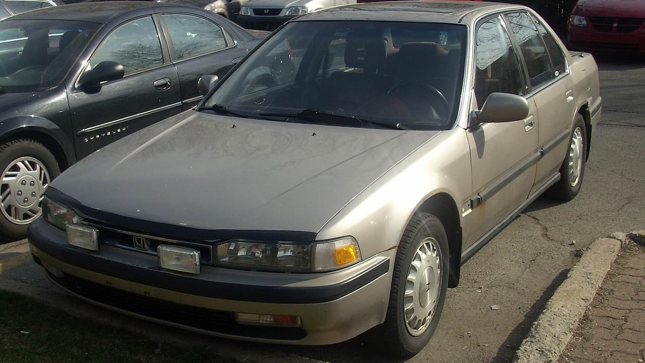Beige 1990 Honda Accord sedan with pop-up headlights parked on street next to other vehicles