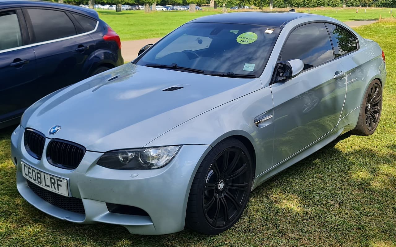Silver 2008 BMW M3 E92 coupe with black wheels parked on grass at outdoor car event