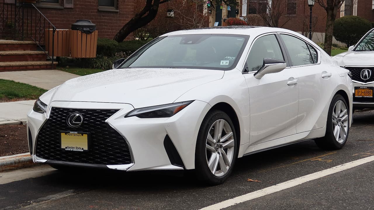 White Lexus IS sedan parked on a residential street, featuring bold grille, sharp headlights, alloy wheels, and a sleek sporty design