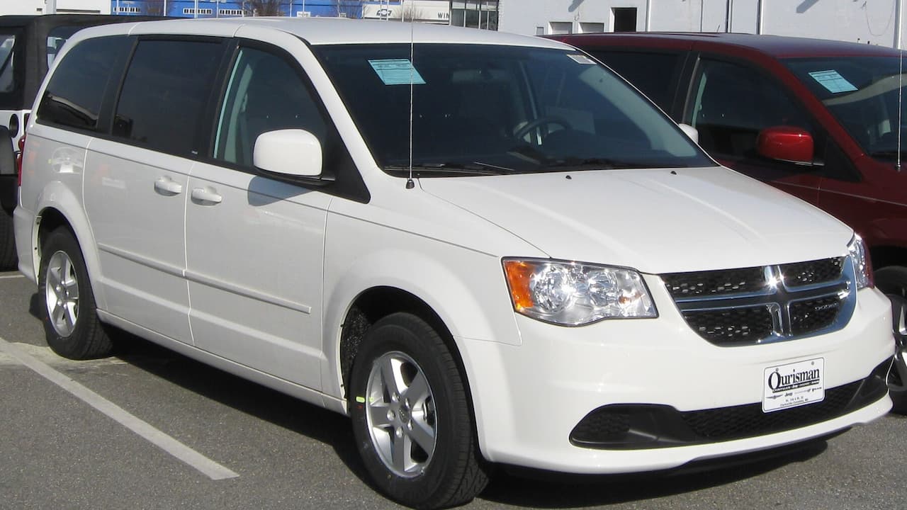 White Dodge Grand Caravan minivan with chrome grille and alloy wheels parked in dealership lot
