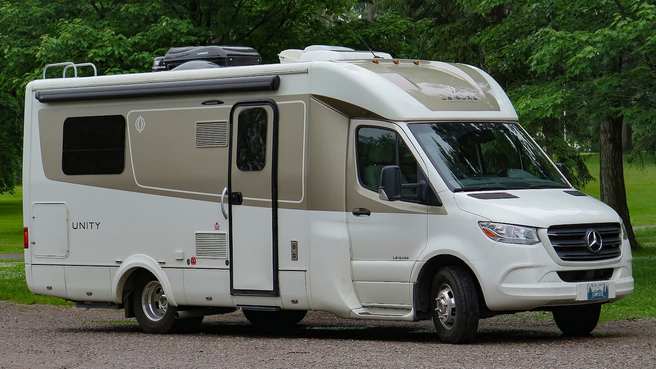White and tan Leisure Travel Vans Unity Class B motorhome with Mercedes chassis parked in green park setting
