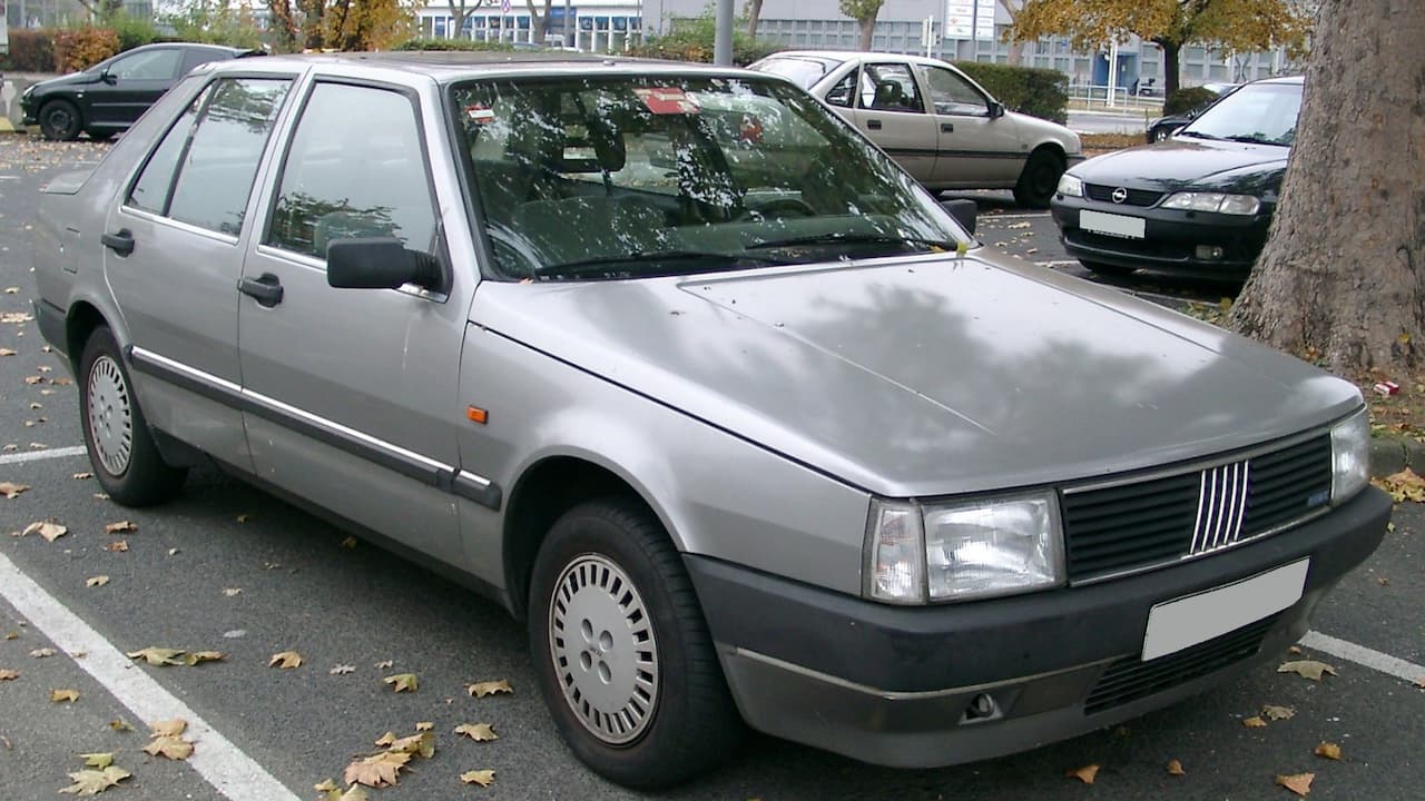 Silver Fiat Croma sedan with distinctive vertical grille parked on street with autumn leaves and other vehicles nearby