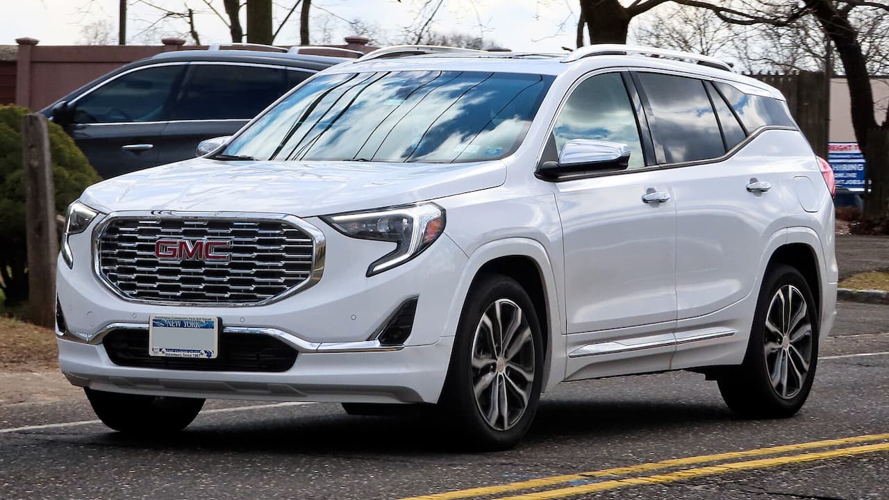 White GMC Terrain SUV with chrome grille and alloy wheels parked on asphalt road with trees nearby