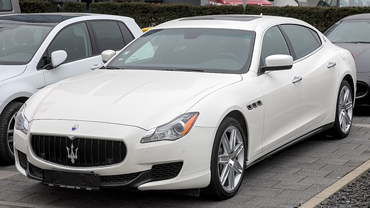 White Maserati Quattroporte luxury sedan with distinctive trident grille parked in outdoor parking area
