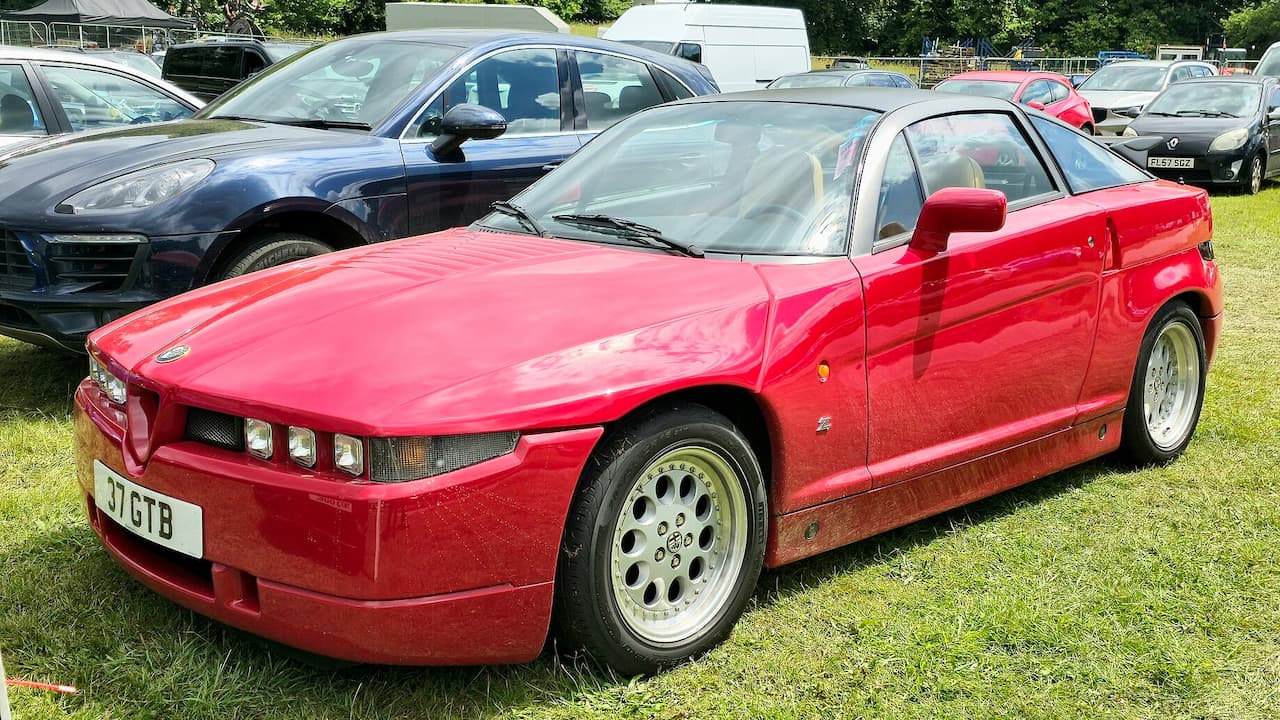 Red Alfa Romeo SZ sports car with distinctive angular design and white alloy wheels at outdoor car show