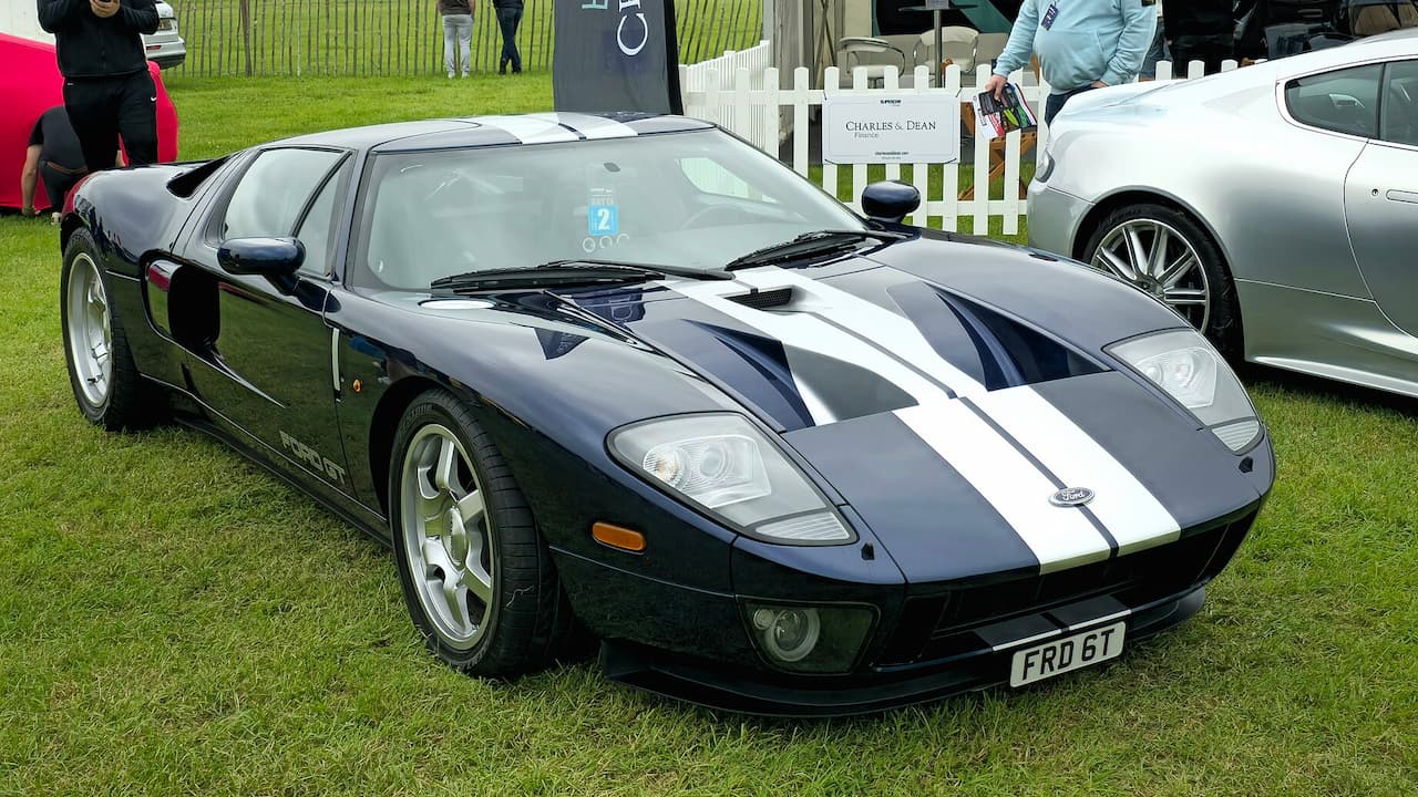 Black 2005 Ford GT sports car with white racing stripes parked on grass at outdoor car show event