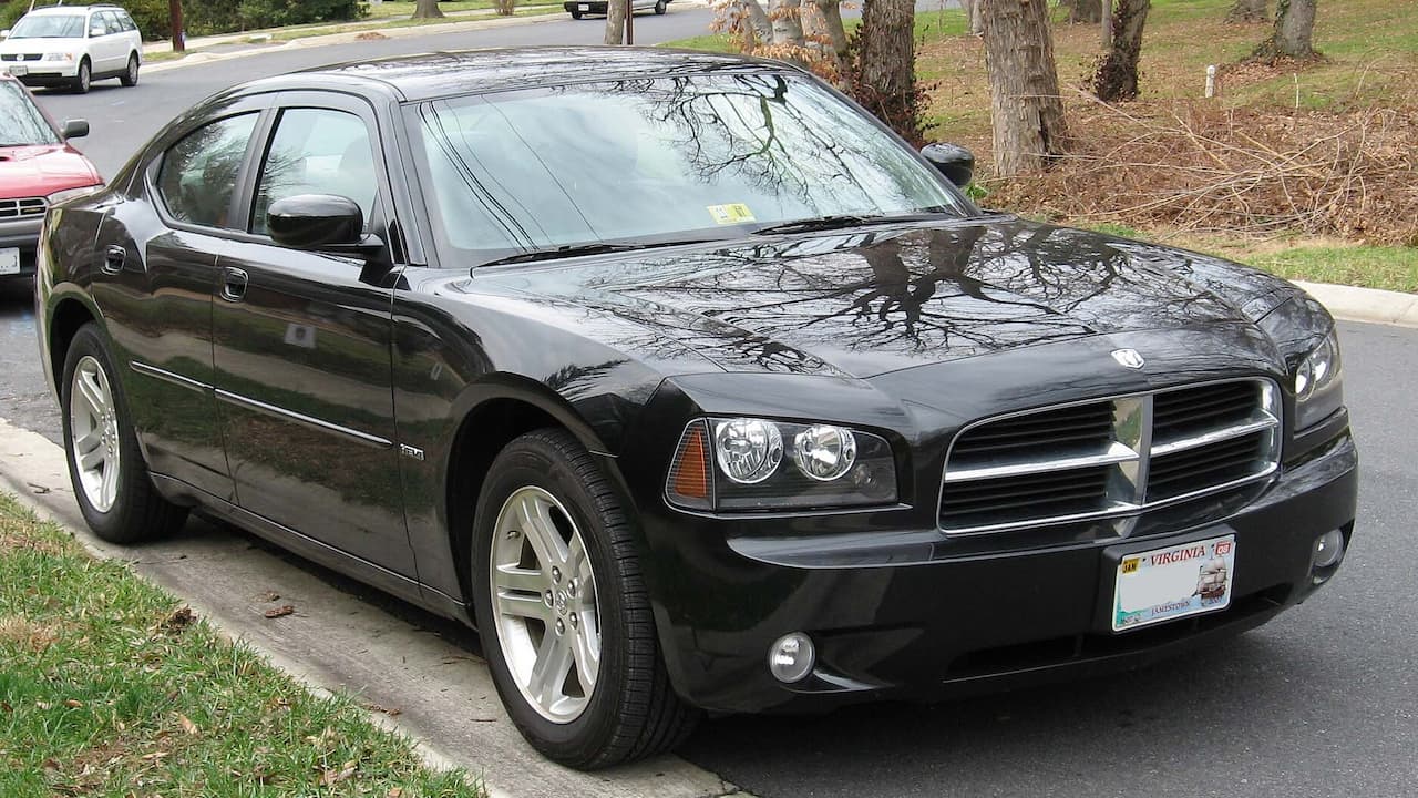 Black Dodge Charger sedan with Virginia license plate parked on residential street beside trees and grass