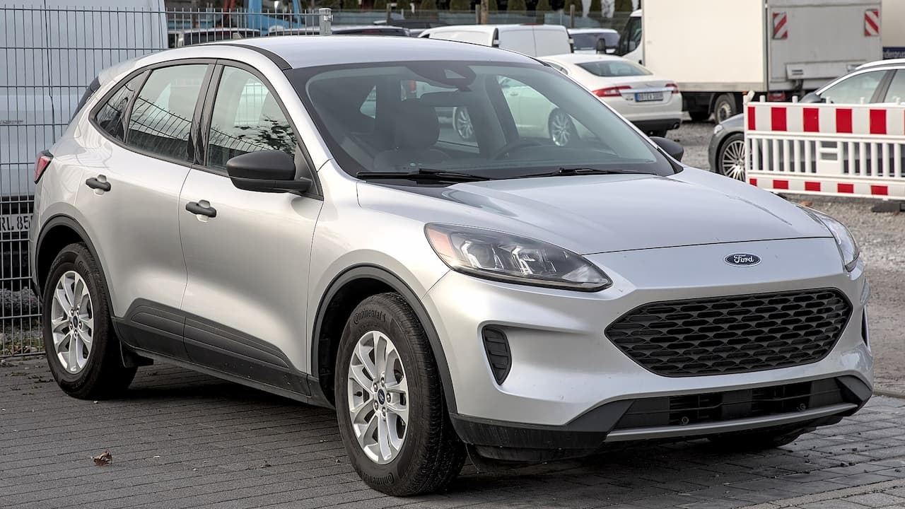 Silver Ford Escape SUV parked on cobblestone street with construction barriers and white van in background