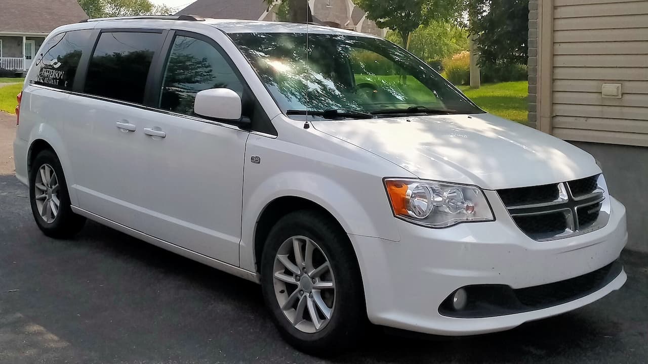 White 2021 Dodge Grand Caravan minivan with alloy wheels and tinted windows parked in residential driveway