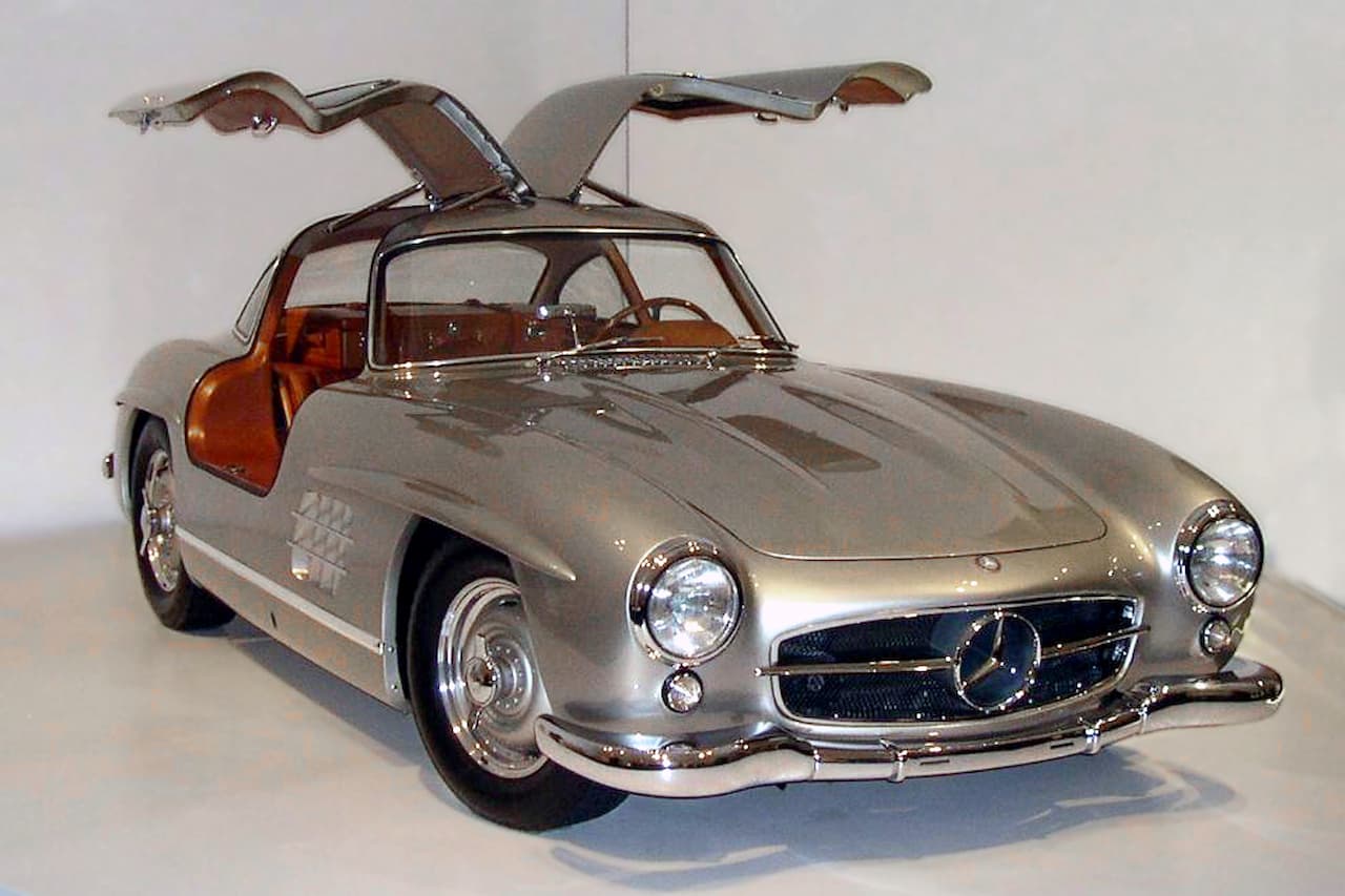 Silver 1955 Mercedes-Benz 300SL Gullwing coupe with iconic upward-opening doors displayed in white museum or showroom setting