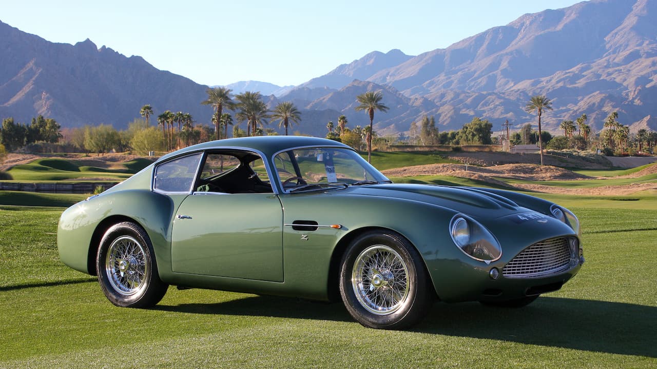 Green Aston Martin DB4 GT Zagato classic sports car with wire wheels parked on golf course with mountains behind