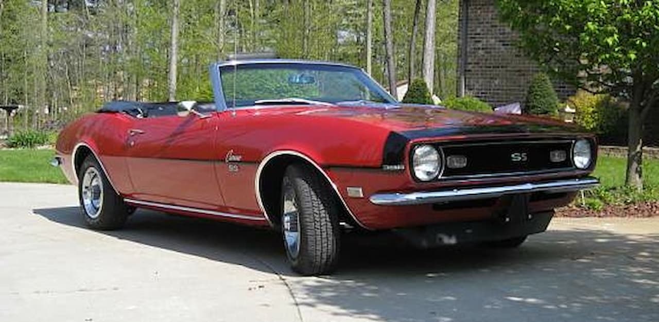 Red 1968 Chevrolet Camaro SS convertible with black racing stripes parked on concrete driveway in residential setting