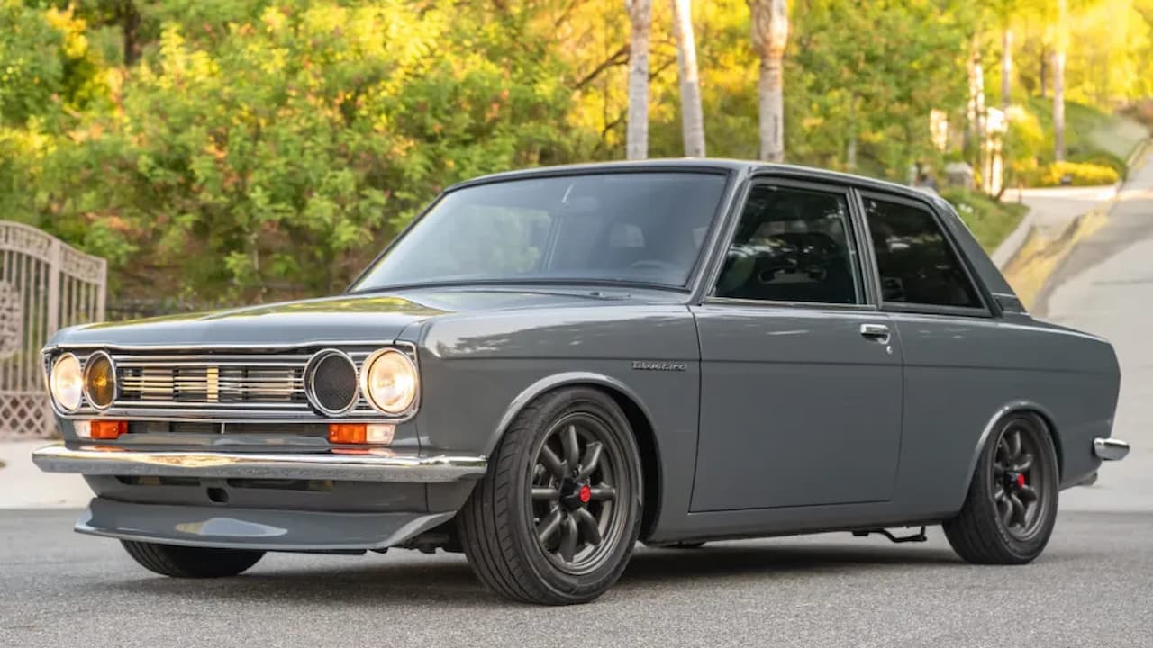 Modified gray 1972 Datsun 510 with lowered suspension, black aftermarket wheels, and round headlights on residential street