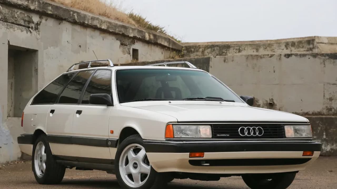 White 1991 Audi 200 Avant Quattro station wagon with roof rack parked against weathered concrete wall background