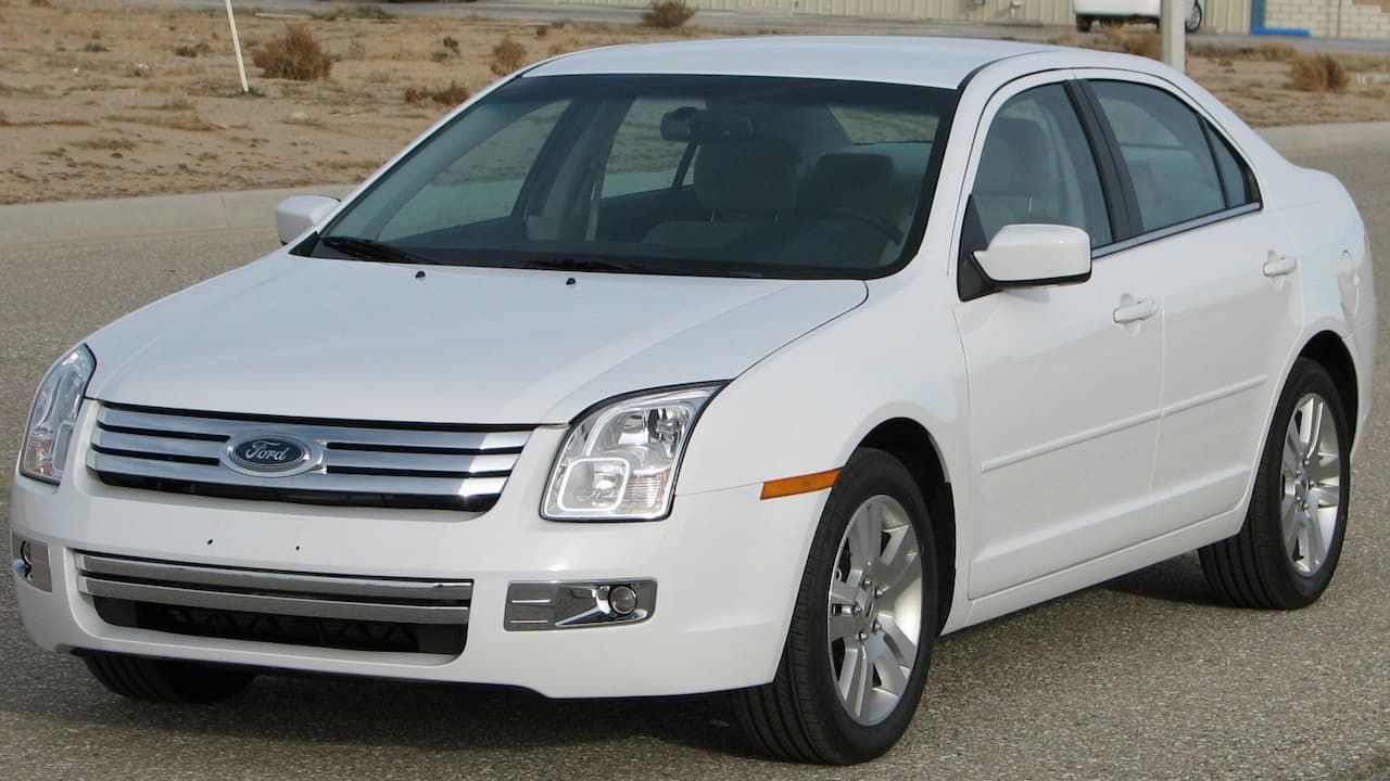 White Ford Fusion sedan with chrome grille and alloy wheels parked on asphalt in desert landscape
