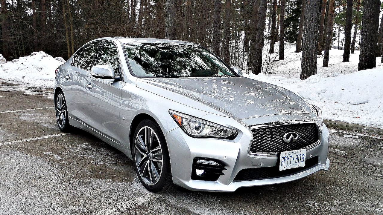 Silver Infiniti Q50 sedan parked in snowy forest setting, featuring chrome grille, LED headlights, alloy wheels, and sleek, sporty lines