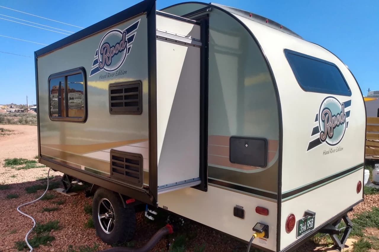 White and gray Forest River R-Pod travel trailer with open door parked in desert setting under blue sky