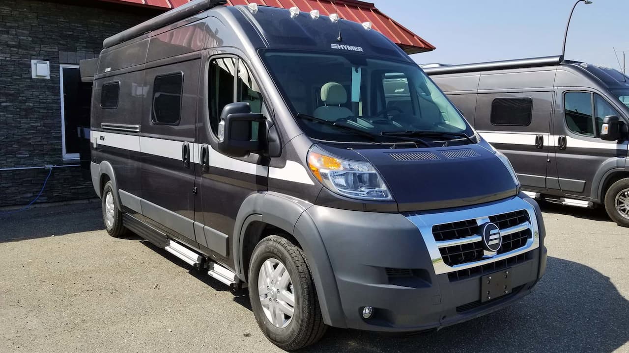Gray Hymer Aktiv Class B motorhome with high-top roof parked at RV dealership with other vehicles