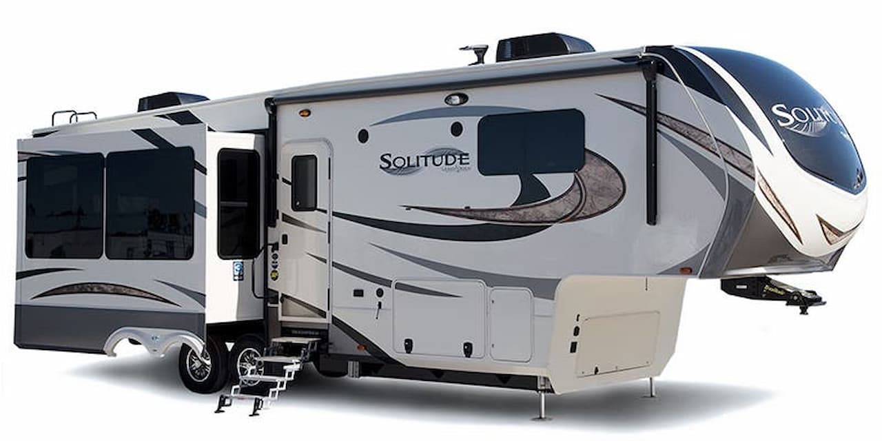 White and gray Grand Design Solitude fifth wheel trailer with slide-outs and stabilizer jacks on white background