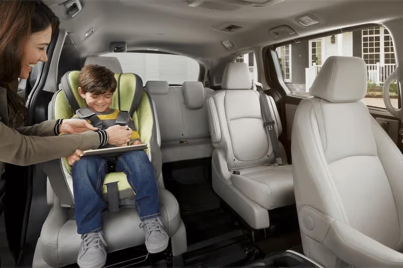 Mother helping child in green car seat inside Honda Odyssey minivan with gray leather seats and spacious interior