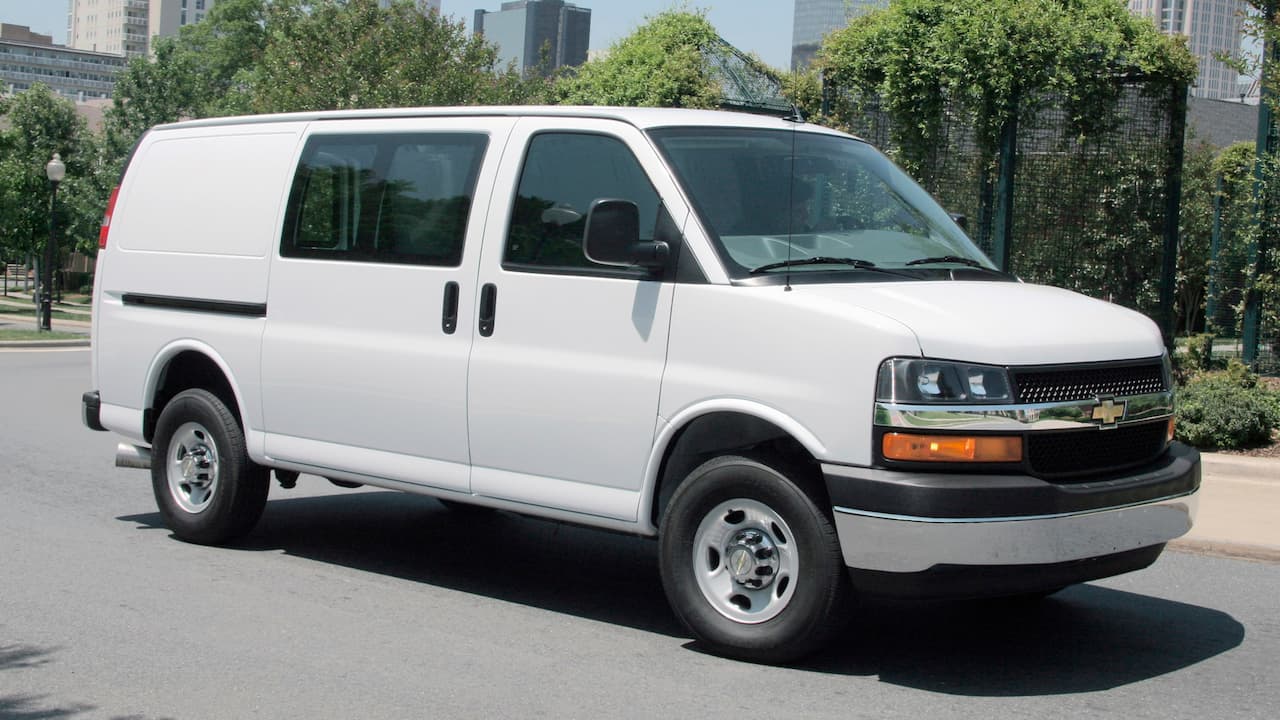 White 2022 Chevrolet Express cargo van with passenger windows and steel wheels parked on city street
