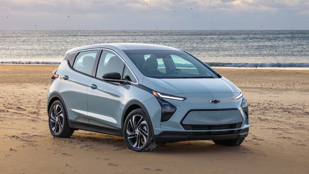 Silver 2025 Chevrolet Bolt EV parked on sandy beach with ocean waves and cloudy sky in background