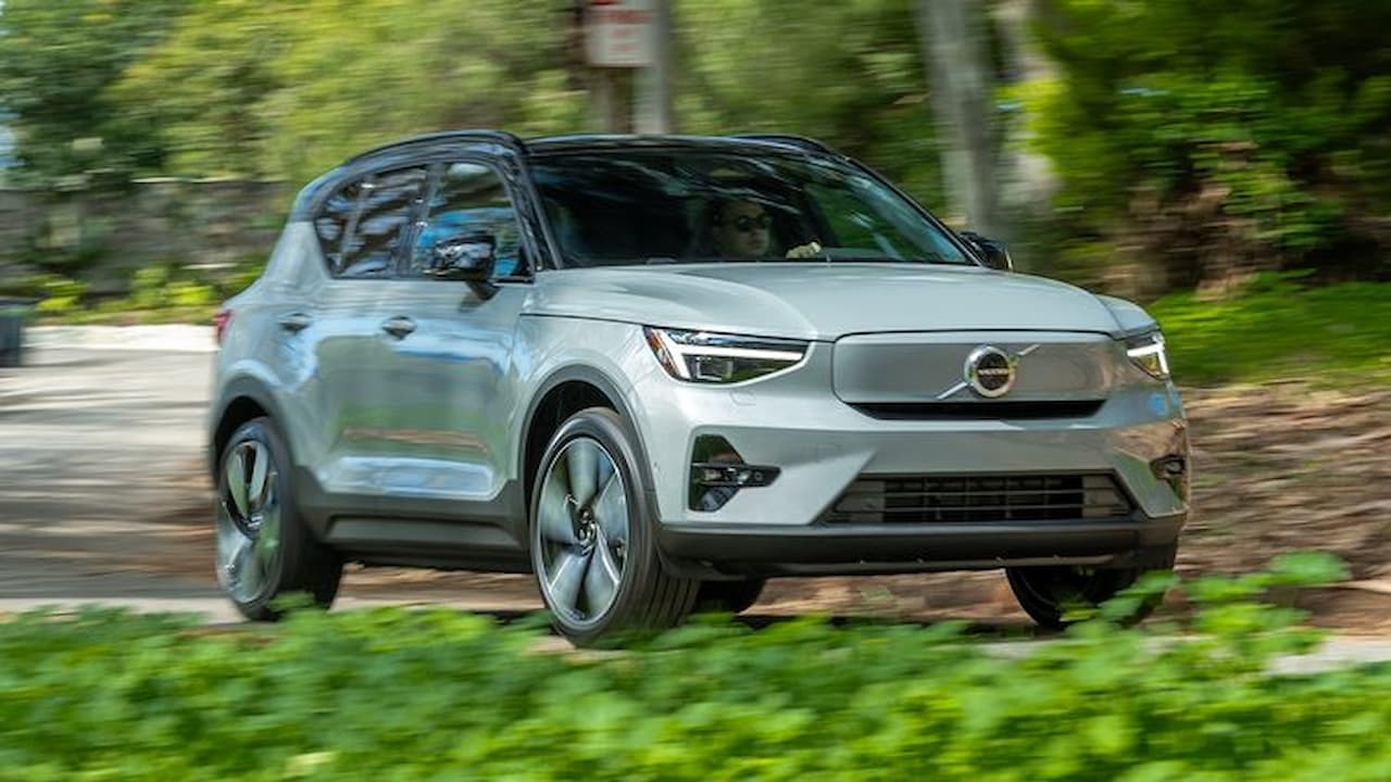 Silver Volvo XC40 Recharge electric SUV driving on paved road with lush green forest vegetation in background