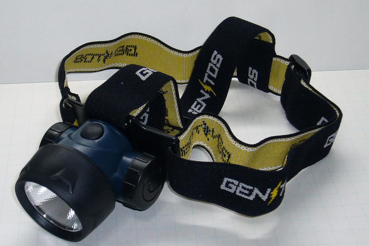 Black LED headlamp with reflective lens and adjustable yellow-black elastic headband featuring brand text on white surface