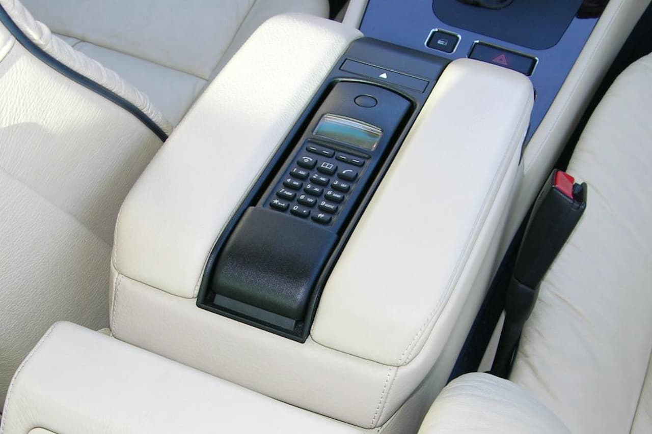 Vintage car phone with numeric keypad and small display screen built into beige leather center console armrest