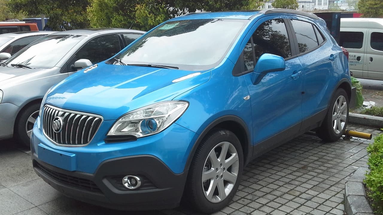 Bright blue Buick Encore SUV with chrome grille and alloy wheels parked on brick pavement in parking area
