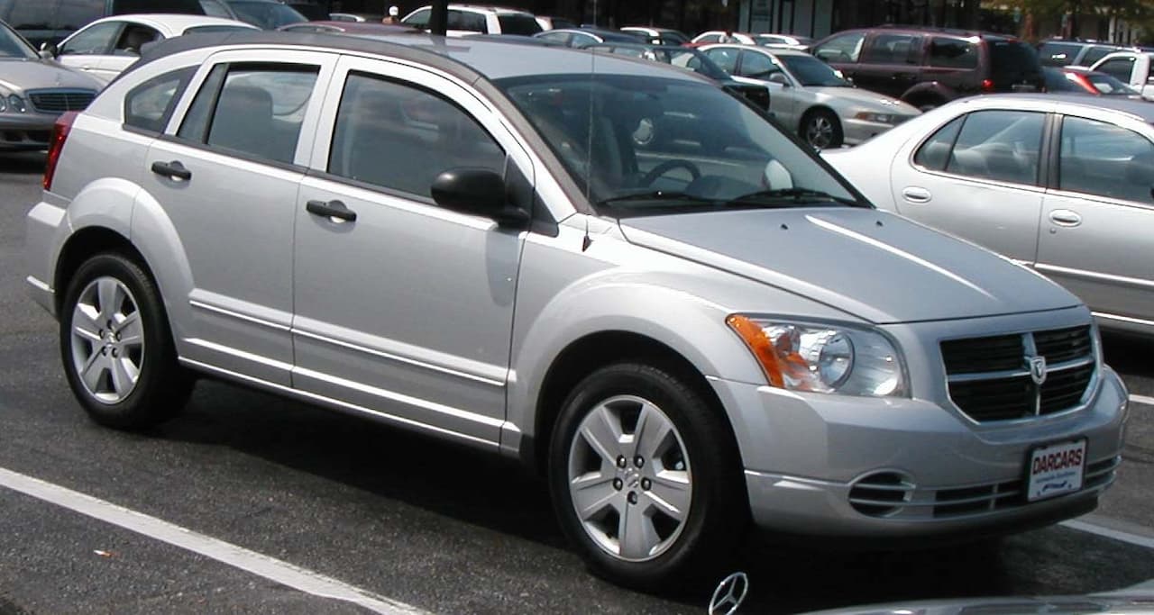 Silver Dodge Caliber compact SUV parked in parking lot with dealer license plate frame among other vehicles