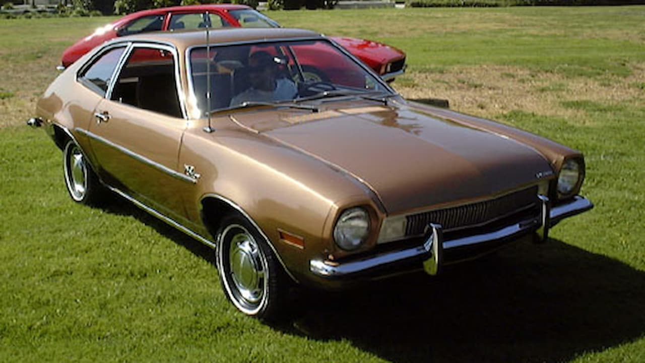 Gold Ford Pinto compact car with chrome bumpers and rally wheels parked on grass at outdoor event