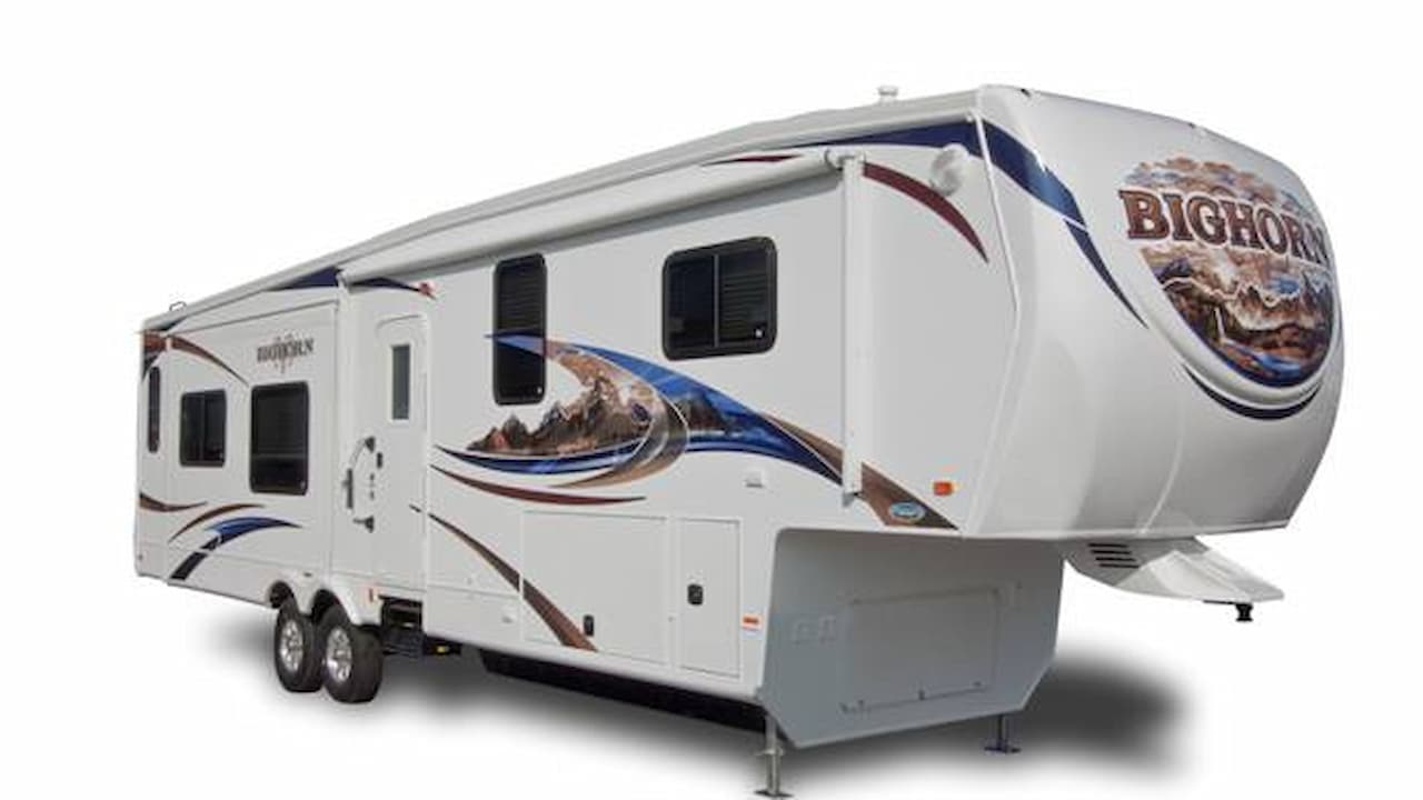 White Heartland Bighorn fifth wheel trailer with mountain sheep graphics and stabilizer jacks on white background