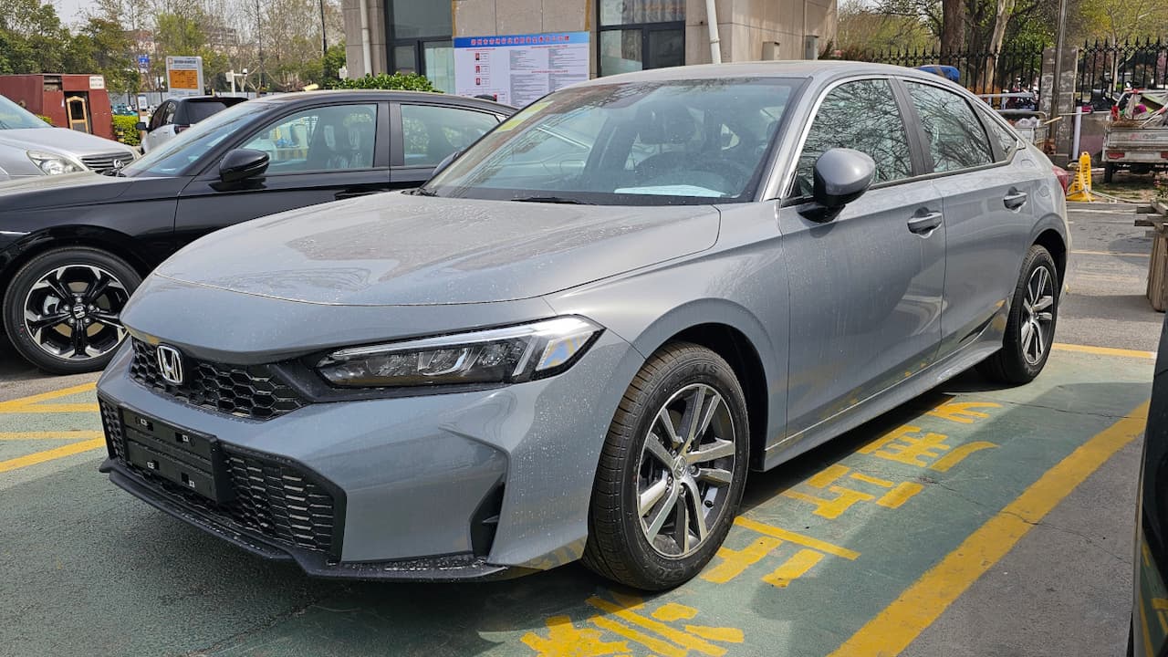 Silver 2025 Honda Civic sedan parked in urban parking lot with yellow lane markings and other vehicles nearby