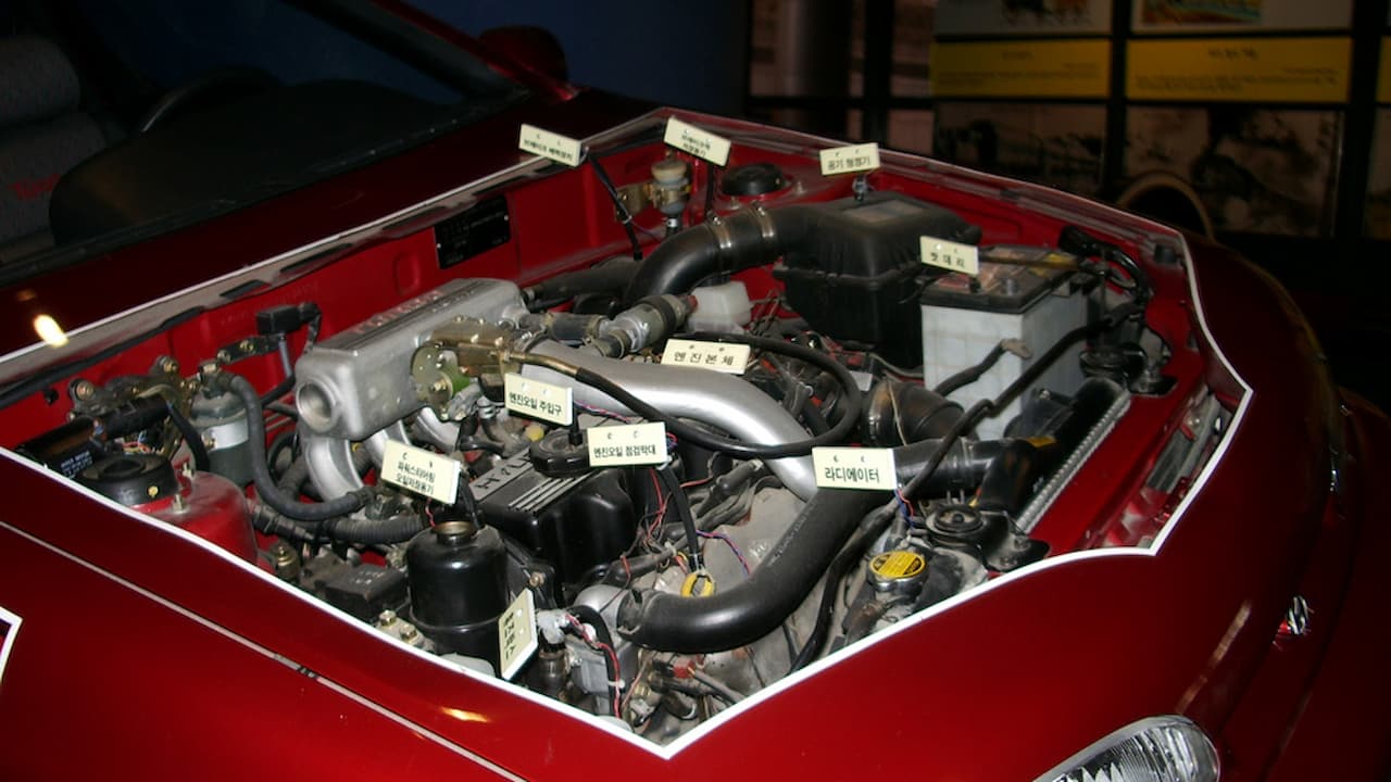 Red car engine bay with exposed turbocharger system, intercooler piping, and labeled components showing upgraded turbo installation