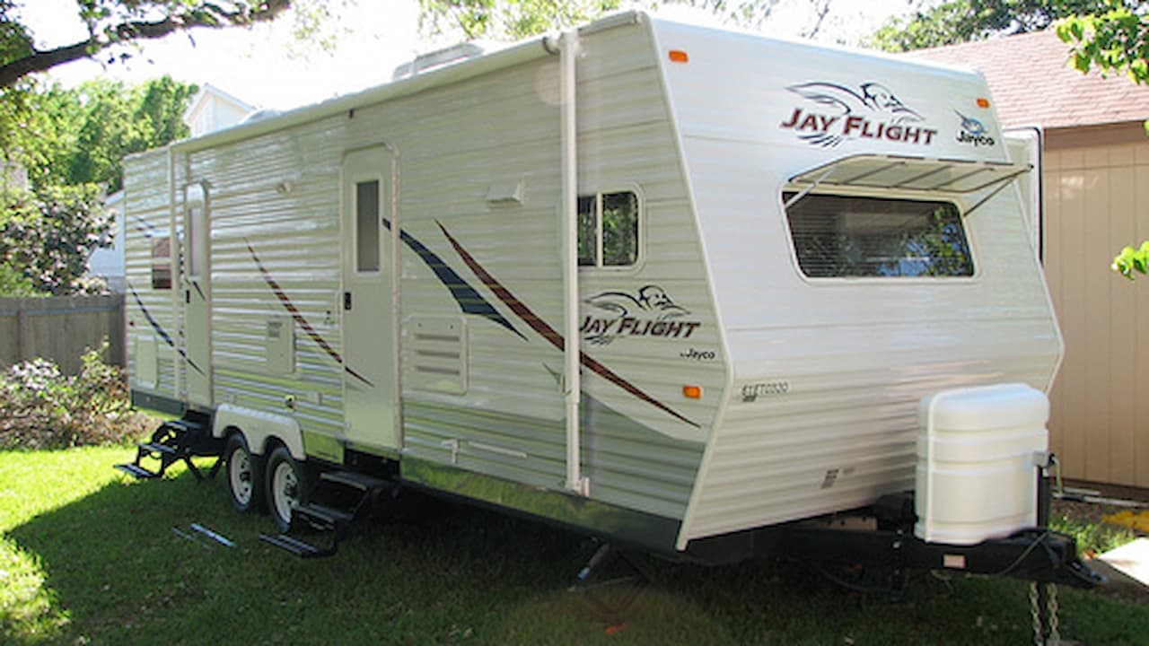 White Jayco Jay Flight travel trailer with awning parked on grass in residential backyard near house