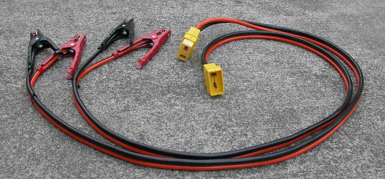 Red and black jumper cables with clamps and yellow connectors laid out on gray asphalt surface