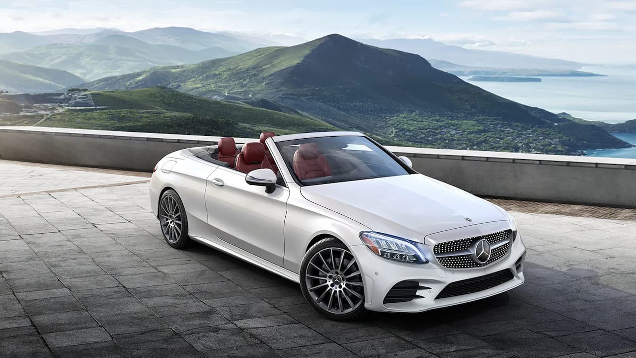 White Mercedes-Benz C-Class Cabriolet with red interior parked on stone terrace overlooking mountains and ocean