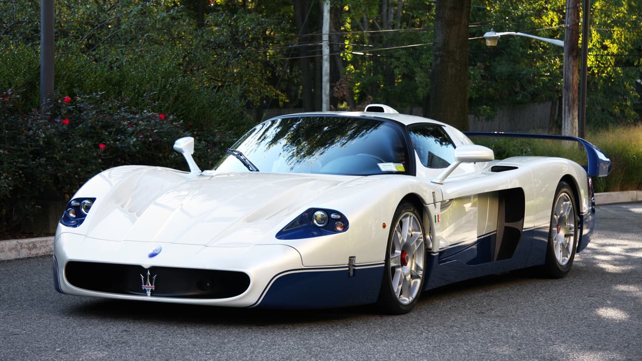 White Maserati MC12 supercar with distinctive aerodynamic design and blue accents parked on residential street