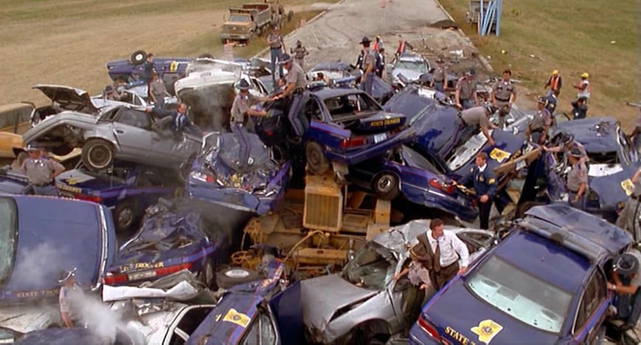 Massive multi-car pileup scene with dozens of crashed police cars and emergency responders examining the wreckage aftermath
