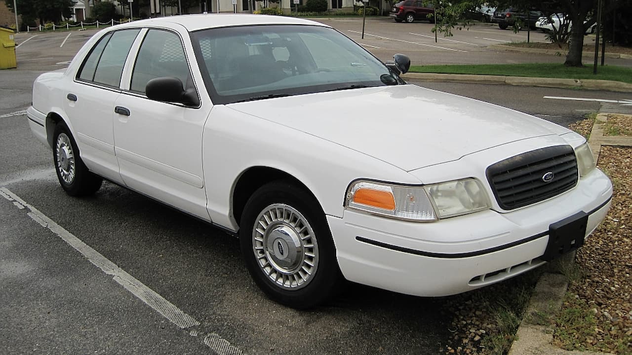 White Ford Crown Victoria police interceptor with steel wheels and hubcaps parked on street in residential area